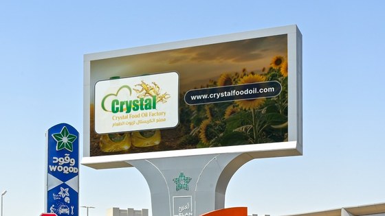 A roadside digital billboard in Qatar carrying the Crystal Food Oil Factory board, with the bilingual Latin and Arabic lockup over a sunflower field.