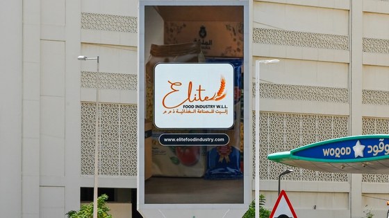 A vertical digital screen on a Doha building showing the Elite Food Industry board with its bilingual lockup and flour packaging.