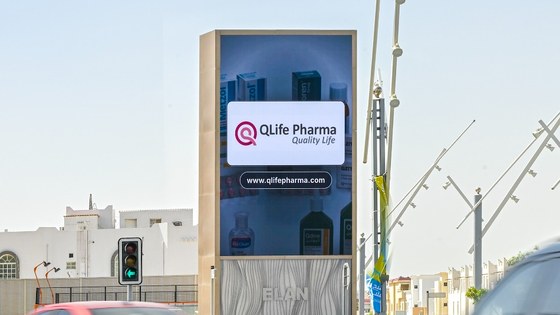 A digital screen at a Doha junction carrying the QLife Pharma board, Quality Life strapline and qlifepharma.com address, on an ELAN Media structure.